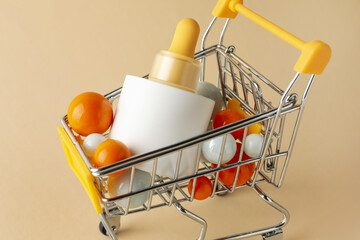 Canvas Print - Bottle of skin care product and colorful balls in small shopping cart on beige background, closeup