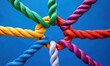 © Natawut - interconnected colorful ropes tied in knots against a blue background. Unity and teamwork concept.