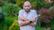 © HI Pictures - A handsome middle-aged businessman looks at the camera with a facial expression that clearly shows that he is cold, in a forested park on a summer day