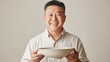 © Sinechana - 26.A portrait of an Asian man with a cheerful smile, holding an empty ceramic bowl with both hands, captured against a softly lit neutral background.