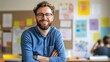 © Sirat - Smiling man with glasses in a bright classroom setting, showcasing a creative atmosphere with colorful charts and students engaged in learning activities