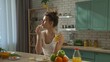 © kinomaster - Young woman at the table in the kitchen preparing spring rolls for healthy lunch, eating fresh spring rolls and drinks orange juice, enjoying the taste.