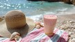 © Kenny Parker - A vibrant tumbler with a strawberry and coconut smoothie placed on a pastel-striped picnic cloth near a woven sun hat and seashells with the ocean nearby