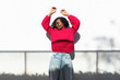 © VISTA by Westend61 - Woman with braids in pink sweater dancing against a white wall