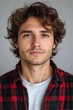 © 3DLeonardo - Close-up portrait of a young man with curly brown hair, wearing a red and black plaid shirt. He has a calm and serious expression.
