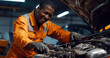 © David Giraud - Mécanicien professionnel afro-américain en uniforme orange souriant et travaillant sur le moteur d'une voiture dans un garage.