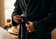 © SERHII - Person tying a belt on dark bathrobe in cozy hotel room with breakfast tray