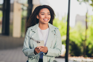 Wall Mural - Charming young woman enjoying a sunny day outdoors in a stylish jacket walking through the vibrant city streets