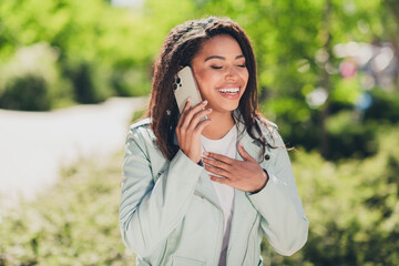 Wall Mural - Young woman chatting happily on her phone while enjoying a sunny day outdoors in casual style