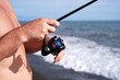 © isavira - Spinning fishing. Close-up of male fisherman hands catching fish with spinning rod at sea on sunny hot day against blue sky background