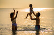 © Hip.hub - Family enjoys a playful moment in the water at sunset, capturing joy and connection on a warm summer evening