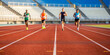© n3wttfoto - Four runners compete on a track in a stadium blurred grandstand view dynamic sports action