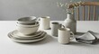 © Nima - Elegant Tableware Set on Neutral Background - Stacked bowls and mugs in neutral tones sit on a table with a linen napkin and a vase of flowers. Perfect for kitchen or home decor