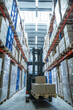© MACO - Fork lift in the middle of large warehouse aisle with large pallets of boxes.