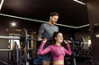 © Mediteraneo - Young woman does shoulder press with weights in the gym while her personal trainer is spotting her.