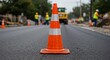 © Yury - Construction cone in the foreground symbolizing safety and caution during a Labor Day road work project featuring workers in the background actively repairing the street