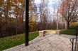 © VIS Fine Arts - A backyard patio with stone pavers and a curved stone wall, framed by black metal railings. Fallen leaves and autumn foliage create a warm, seasonal atmosphere