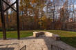 © VIS Fine Arts - A backyard patio with stone pavers and a curved stone wall, framed by black metal railings. Fallen leaves and autumn foliage create a warm, seasonal atmosphere