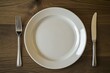 © Phuriphat - A white plate with a fork and knife on a wooden table