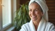 © miss irine - Happy middle aged woman in bathrobe with towel on head looks at window. Smiling mature lady at spa, enjoying skincare, wellness, beauty routine, detox treatment. Anti-aging procedure for face, body.