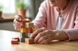 © miss irine - Faceless elderly woman with dementia plays wooden blocks on table, developing motor skills. Senior patient builds tower in geriatric clinic. Game for brain training, memory improvement, cognitive