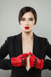 © millaf (Nemchinova) - Gorgeous fashionable woman with make-up and dark hair wearing red leather gloves and black suit posing indoor