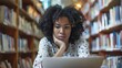 © Galib - A young Black woman is working on a laptop in a library, with a serious expression.