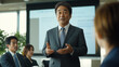 © bephoto - 日本の企業の朝会でリーダーが社員に向けて話すシーン