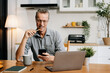© NINENII - Lifestyle people, using laptop computer and smartphone sitting in the kitchen. Happy mature male, entrepreneur, small business owner working online at home office.