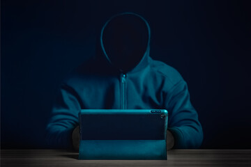 a mysterious figure in a dark hoodie uses a tablet in a dimly lit setting, representing cybercrime, 