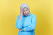 © Iqy - A stressed asian woman in a brown hijab holds her head with closed eyes, feeling overwhelmed.