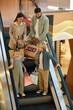 © DragonImages - Vertical high angle shot of Caucasian family holding big paper bags with new toys and clothes standing on escalator in shopping mall