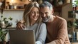 © Oleksandr - Mature couple enjoying quality time together at home while browsing on laptop, sharing intimate moment in cozy kitchen setting with warm lighting and plants