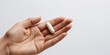 © Natsumae - A single white pill rests gently in the palm of a hand, against a clean white background.  A moment of quiet contemplation, health, and wellness.