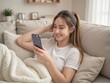 © Joedifries - joyful woman lying on a couch at home, smiling brightly as she uses her cellphone, with a relaxed and content expression.