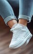 © Fathor - Close-up of white sneakers on the feet, jeans, and socks on an office desk, legs in a motion pose. Close-up of a young woman's foot wearing casual shoes. White sports shoe close-up on a modern home