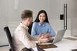 © fizkes - Professional consultation. Confident young businessman sitting at office table consulting young Asian female client colleague explain project agreement details using notebook pc express expert opinion