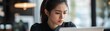 © Natty - A young woman sits at a wooden desk, gazing intently at her laptop screen. Her brow is furrowed, and her lips are slightly pursed, reflecting a deep sense of sadness and concern.