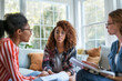 © ExF Designs - Three Women Engaged in a Discussion While Holding Paper Documents.