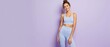 © schiers_images - Fit young woman in lavender workout clothes standing confidently on a solid purple background.