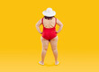 © Studio Romantic - Full body photo of a funny fat overweight woman in red swimsuit and beach hat standing back with hands at sides isolated on studio yellow background. Summer holiday trip and vacation concept.