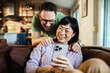 © Marko Geber - Happy couple laughing while looking at smartphone at home