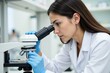 © SimpleDesignStudio - Focused Young Hispanic Female Scientist in Laboratory Coat Examining Specimen Through Microscope in Modern Research Laboratory Setting