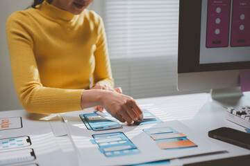 Wall Mural - female web designer creating mobile app wireframes on paper prototypes while arranging layout framew