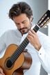 © PaulShlykov - Man playing classical guitar indoors with focus and passion in a well-lit modern space