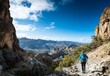 © BerkahStock - Hiker trekking scenic mountain trail, vast valley view.