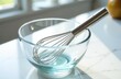 © Sergey - Glass bowl and stainless steel whisk on white marble countertop