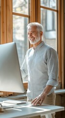 Aufkleber - Smiling older man working at a desk with a computer in a bright, minimalist workspace near large windows