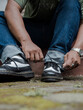 © Yasuspade - Detail of vintage wing-toed brogue shoes shining on a mossy block. Close-up view of a man tying black and white genuine leather brogue shoelaces outdoors.
