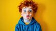 © hdesert - A playful and colorful portrait of a young freckled boy with messy red hair, wearing a bright blue hoodie, making a funny face against a yellow background